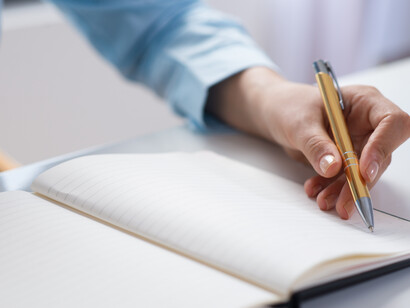 Una persona scrive con una penna dorata su un quaderno aperto