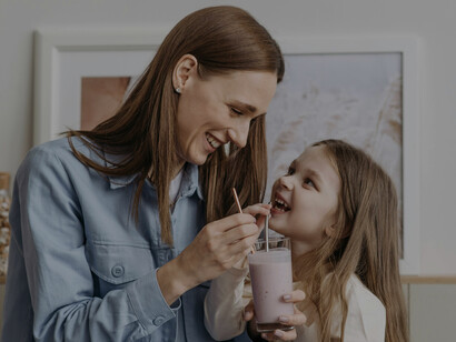 Child and mother making and sharing a strawberry smoothie