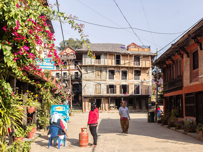 People walking along the streets lined with concrete buildings in Bandipur, Nepal, on a sunny day