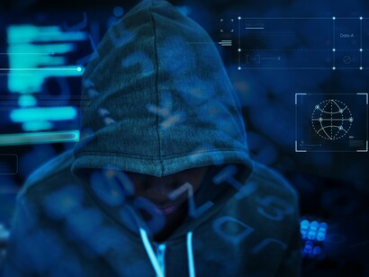 A hooded figure with code running behind them, representing how cyberterrorism can strike without warning and cause widespread chaos and disruption