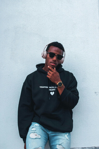 In Hampton, VA, a Black man poses in a hoodie as he rests against a white wall, USA