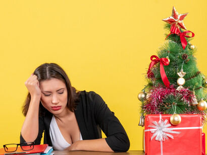 A candid home scene of an exhausted and nervous young woman sitting at a table near Christmas decorations during stressful holiday preparations