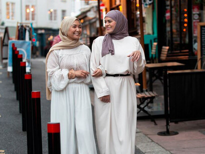Women in hijabs smiling and chatting as they stroll down the street