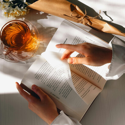 Woman holding a book with a cup of tea and daffodils beside her