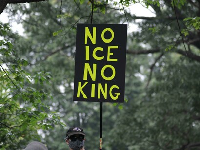 Protest sign at an ICE demonstration in Baltimore, Maryland, United States, framed by trees and greenery