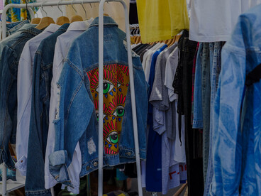Secondhand fashion on display at a flea market, with clothes hanging in a colorful, textured close-up that highlights reuse and individuality