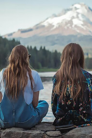 Two women sitting on the rock and looking at the water and mountain 