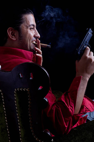 A man seen from behind, seated in an armchair with a cigar in hand, symbolizing power and mystery