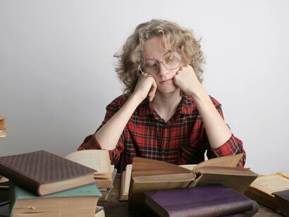 Rapaz lê cercado por muitos livros. O Livro, não importa se impresso ou digital, faz o trabalho digno de tornar o indivíduo melhor como pessoa, aumenta o seu vocabulário, cria novos horizontes e derruba os limites, muitos deles mentais e não físicos