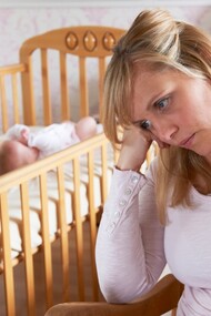 Una madre con síntomas de depresión junto a la cuna de su hijo recién nacido