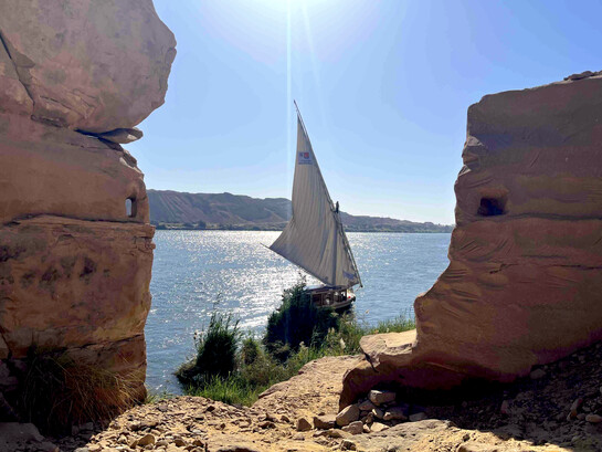 Gebel el-Silsila with rock-cut loopholes overlooking the Nile, as a felucca sails past in Egypt