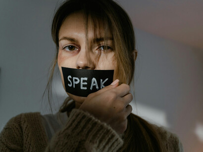 Bruised woman tearing tape from her mouth — a powerful image of silenced voices resisting authoritarian control