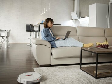 A resident working as a robot vacuum tidies the room, highlighting the evolution of everyday domestic comfort