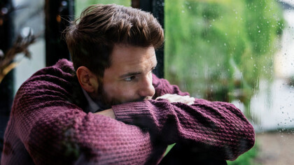 A heartbroken man, looking through the window on a rainy day, waiting for his lover to come back home