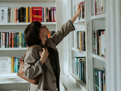 Mulher escolhe livro em estante. O local versus o global, onde por um lado apreciamos o local, a tradição, os costumes, mas por outro lado queremos o fervoroso sangue das pessoas, da tecnologia entre nós