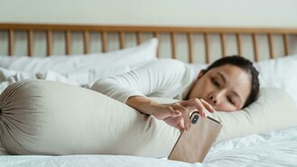 An Asian woman lying in bed while using her smartphone