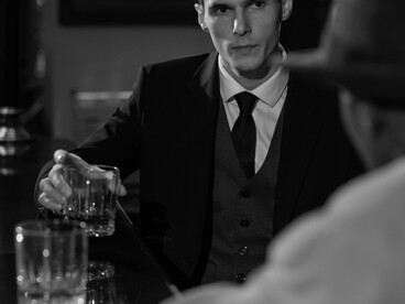 A monochrome photograph showing several men seated at a bar counter
