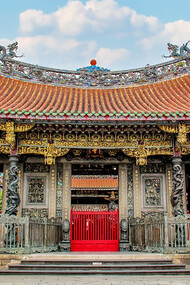 The Longshan Temple in Taipei, Taiwan, features an ancient roof adorned with dragons, set against a backdrop of a clear blue sky and fluffy white clouds
