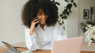 A Gen Z woman sits in front of her laptop and tablet, multitasking between work and digital tasks, and speaking on the phone