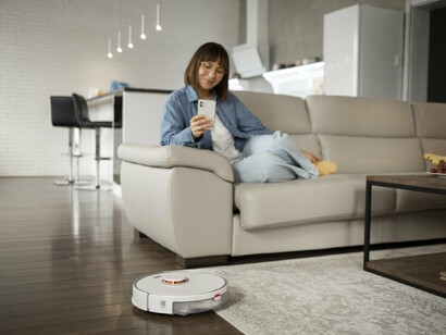A modern living space where a robotic vacuum operates independently as the homeowner checks their phone, conveying the ease of automated home maintenance