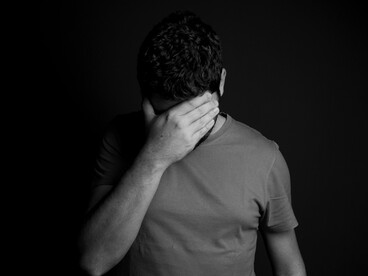 Grayscale photo of a man with his face buried in his hands, showing signs of overwhelming stress