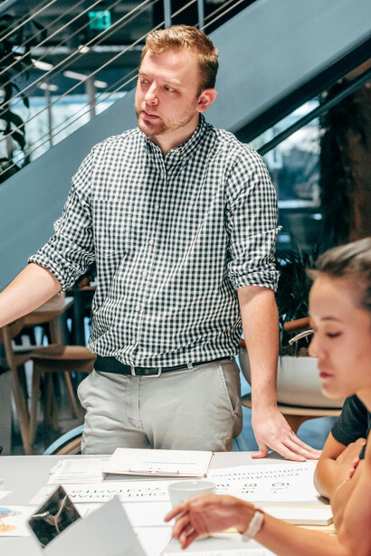 At a startup meeting, a man in a black and white shirt is seated next to a woman in an orange tank top