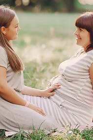 A woman is touching the belly of another pregnant woman, helping her