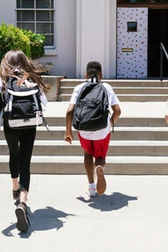 A diverse group of happy students running joyfully toward school