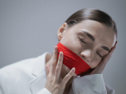 Dressed in a white coat, a woman with a gagged mouth becomes a striking symbol of muted voices and the stillness of suppressed expression