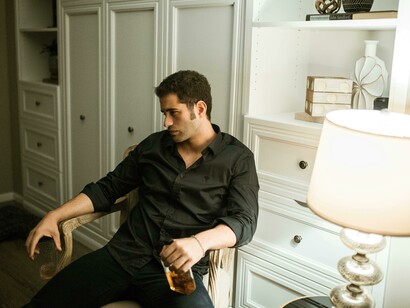 A man sits on the couch with a bottle of alcohol, lost in thought—a quiet reflection of habit