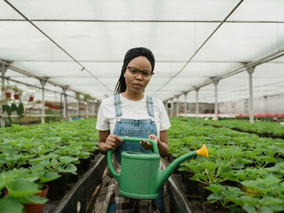 A woman with a green watering can, gazing at the camera, symbolizing agriculture, agronomy, and the broader agricultural industry