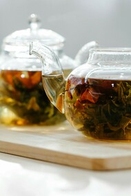 Two glass teapots filled with blooming tea flowers on a light wooden tray