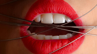 A close-up photo of a woman wearing red lipstick with gray cables across her mouth