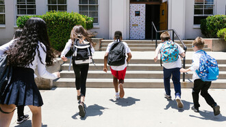 A diverse group of happy students running joyfully toward school