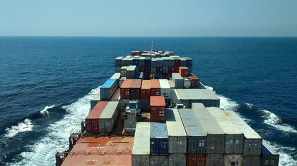A red and white cargo ship sails across the sea during daytime, heading toward a new destination