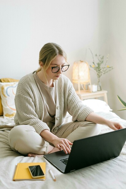 A sedentary moment: woman sitting on bed using a black laptop for extended screen time
