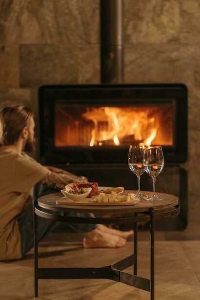 Wine glasses and a warm meal sit on a wooden table, adding to the cozy ambiance near the fireplace