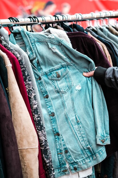 A person holding a shirt in front of a rack filled with second-hand clothing at a charity shop, showcasing sustainable fashion choices