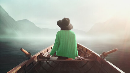A woman in nature, seated on a boat, embodying the journey to self, mindfulness, and the freedom of life beyond professional roles