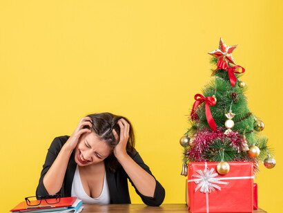 An exhausted and anxious young woman sitting at a table beside Christmas decorations, capturing the stress of holiday preparation