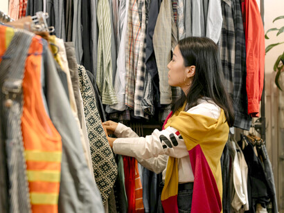 Dressed casually in denim and white, a woman shops thoughtfully in a secondhand fashion store