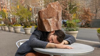 Uomo addormentato su un tavolo da esterno con una grande roccia sulla testa: "Percepisci il peso della giornata sulle spalle, contratte... Il sistema nervoso parasimpatico ti porta in modalità “protezione”: spegne tutto per permetterti di riposare"
