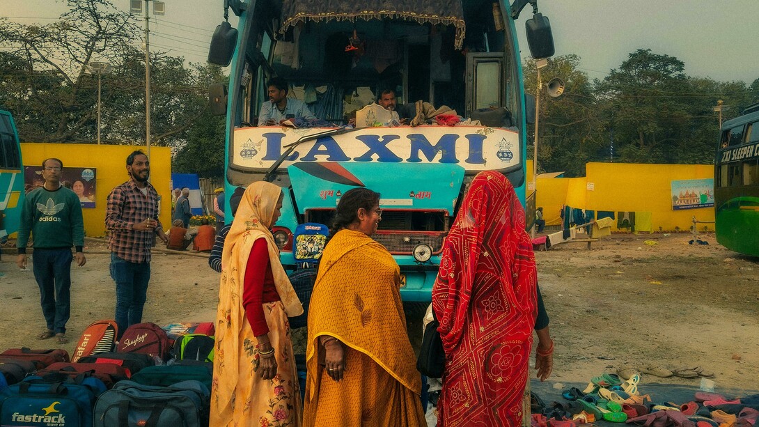 An Indian bus station filled with colorful buses and waiting passengers