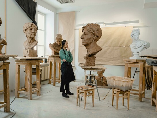 A sculptor works in his art studio, surrounded by tools and unfinished pieces