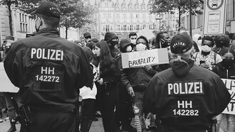 Protesters holding signs that read 'Police Brutality' stand defiantly in front of a line of police officers