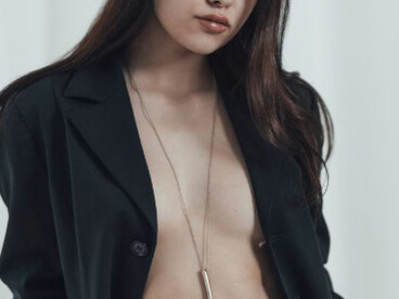 A woman confidently poses in a black suit, wearing nothing underneath