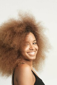 A woman with voluminous hair smiling, showcasing the beauty of natural texture and self-love—celebrating the uniqueness of coily and texturized hair