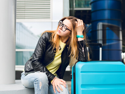 Young woman in glasses with long hair sits near the airport, appearing upset