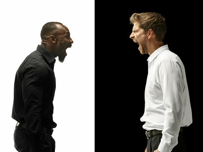 Two men, dressed in starkly contrasting black and white, stand face to face, locked in a heated argument, embodying the oppositional forces that, through mediation, shape transformation and resolution