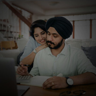 An Indian couple calculating their living expenses, using a calculator and writing notes to manage household finances